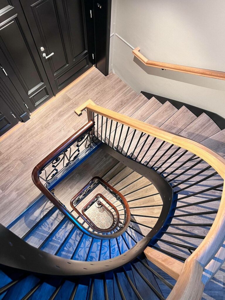 Innendørs spiraltrapp med tregulv og mørke rekkverk, sett ovenfra