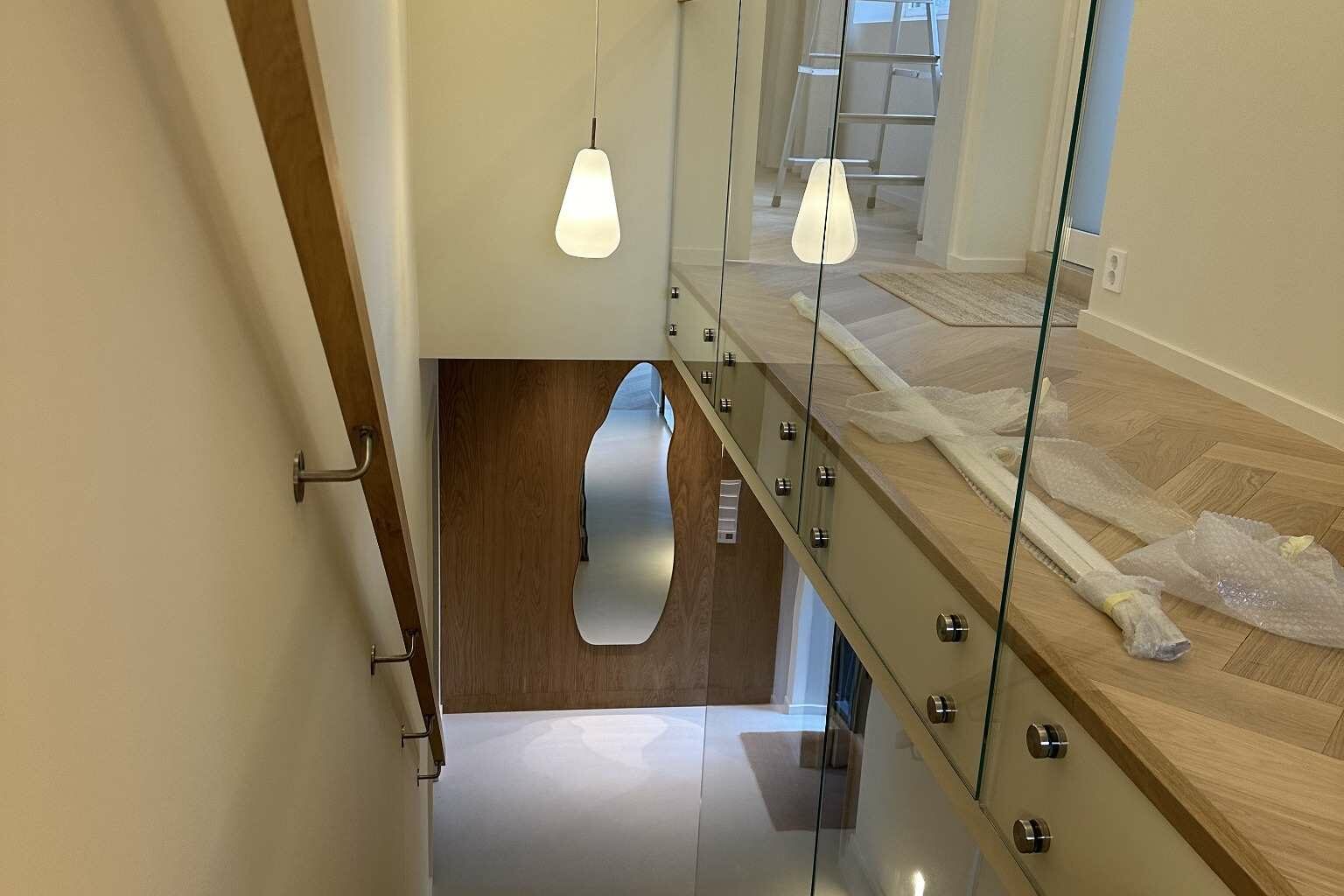 Eiketrapp sett ovenfra med glassrekkverk og hengende lamper.