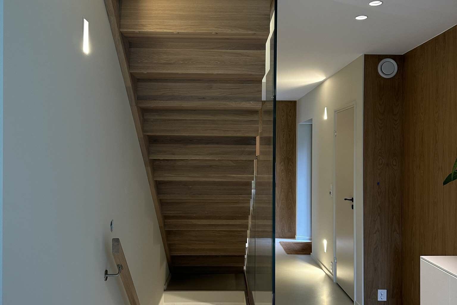 Eiketrapp med glassvegg og trepanel i lys gang.