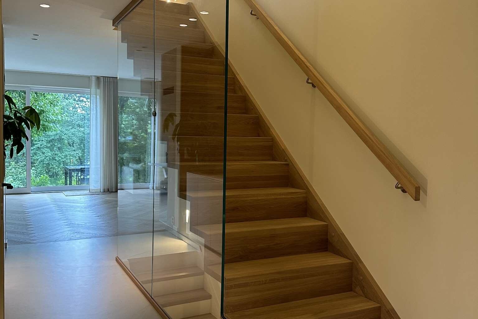 Eiketrapp med glassvegg i lyst og moderne gangområde.