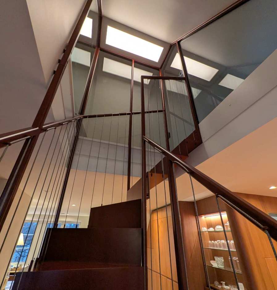 Nærbilde av ståltrapp med tynne vaierer og glassfelt mot toppen.