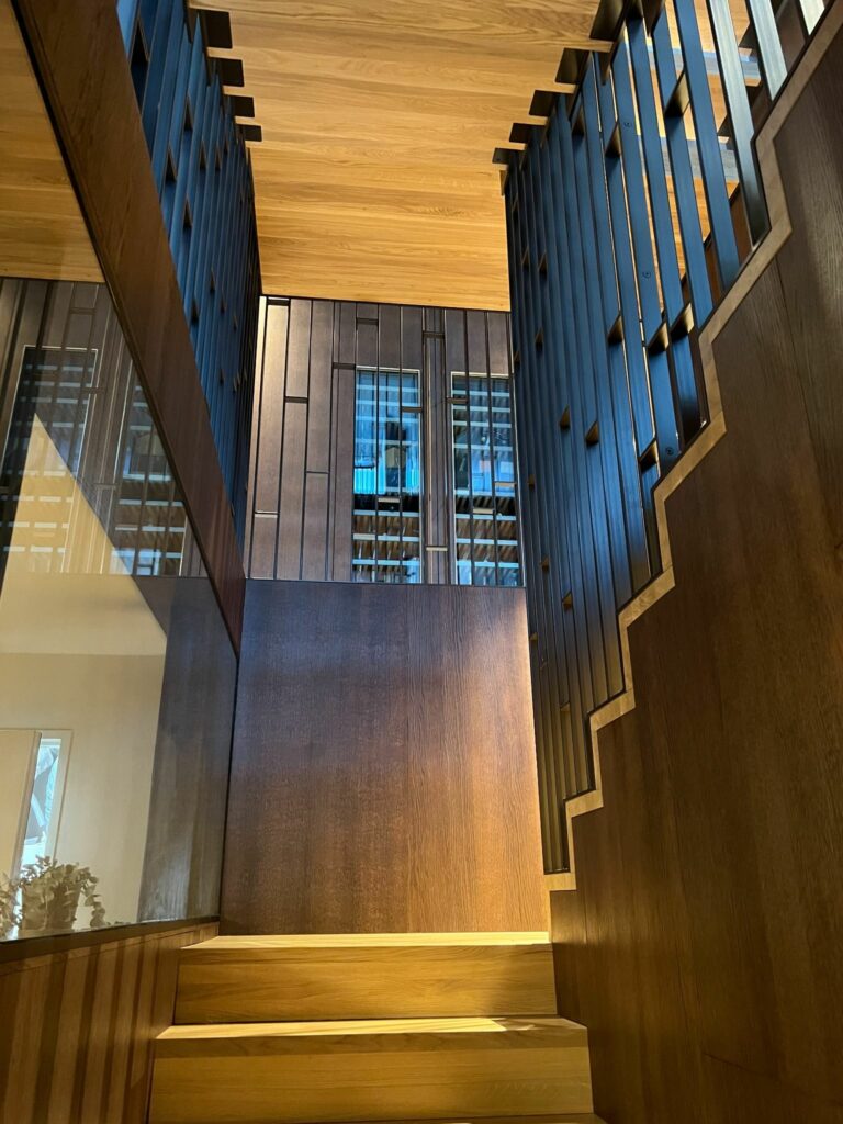 Oppoverperspektiv av designtrapp med eiketrinn og sort metallrekkverk i et moderne bygg med trepanel.